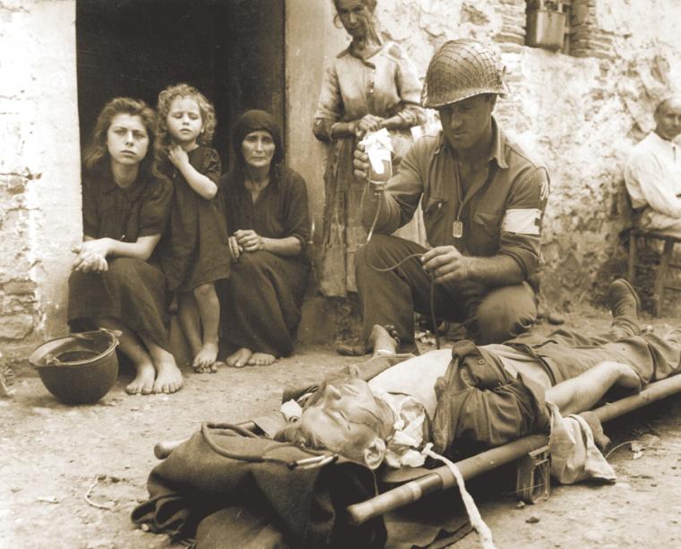 A soldier cares for a wounded man in Sicily.