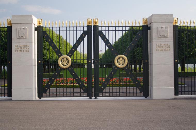 Stone columns flank iron gates with gold seals at the entrance to St. Mihiel American Cemetery.
