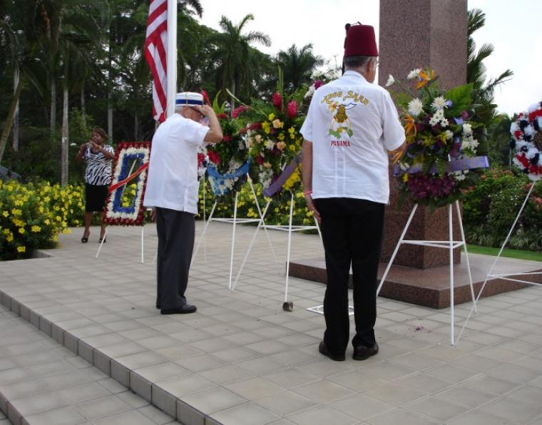 Men stand facing floral wreaths.