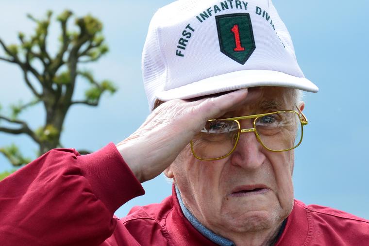 WWII veteran, with a 1st Infantry Division hat, salutes. 