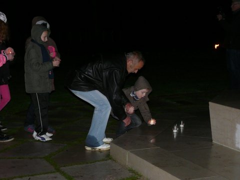 A man and child place candles at the base of the flag pole. 