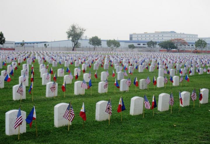 Rows of headstones are adorned with American and Filipino flags.