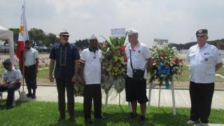Men stand next to the stands holding the floral wreaths. 