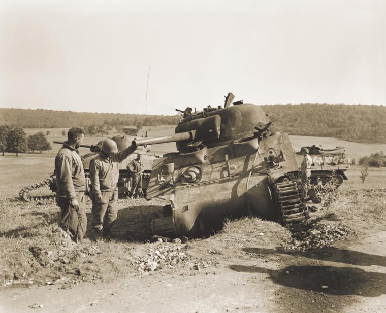 Two soldiers view an M4 tank damaged by German gunfire, September 12, 1944.