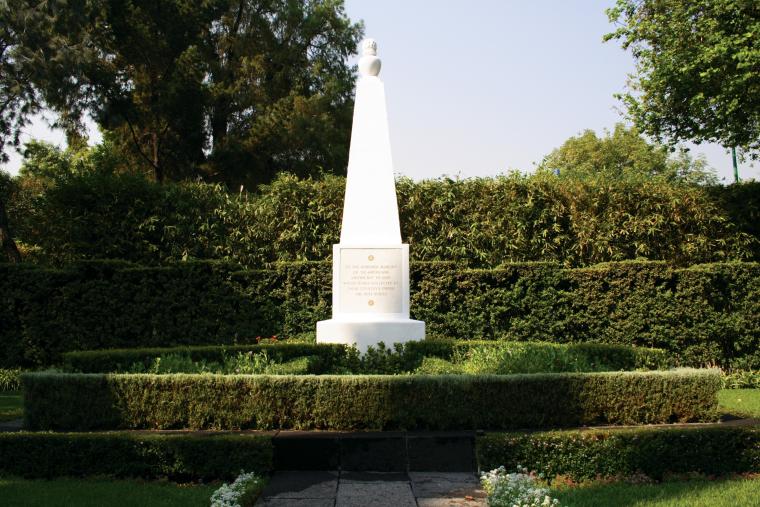 A small white monument at Mexico City National Cemetery sits among bushes.