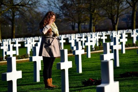 A woman salutes a headstone with a wreath.