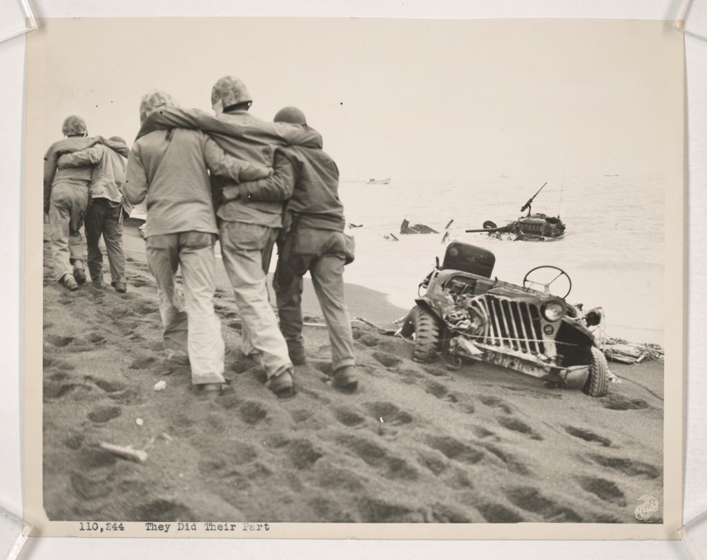 They did their part - Wounded Marines are helped to an aid station by Navy corpsman and Marine walking wounded. The volcanic sand that proved such an obstacle to the landings on Iwo is best illustrated by the depth to which the Jeep at the right has sunk, as well as the deep footsteps of the men going along the beach. U.S. Marine Corps phot by Cpl. Eugene Jones (National Archives)