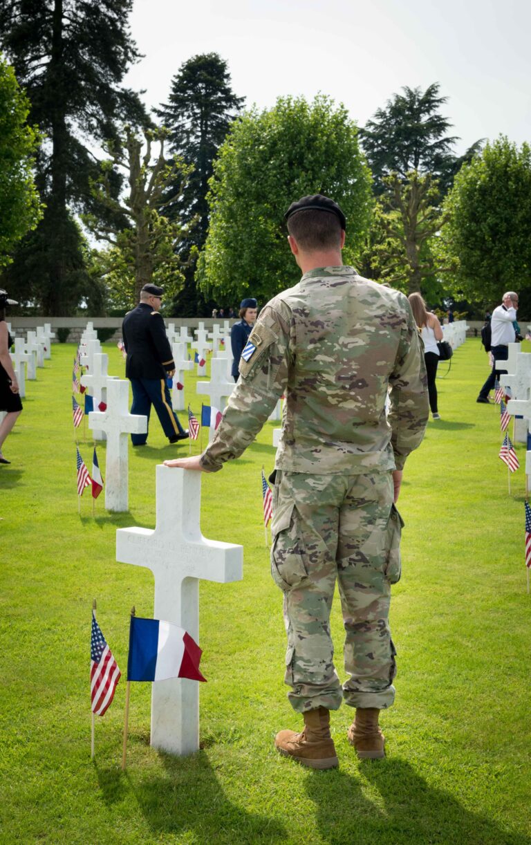 An American soldier stands next to a headstone at Somme American Cemetery. Photo credit: Chantal Mistral-Bernard/American Battle Monuments Commission.