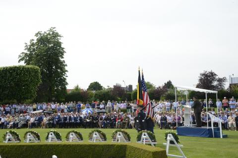 Attendees stand and sit while a man speaks from the podium.