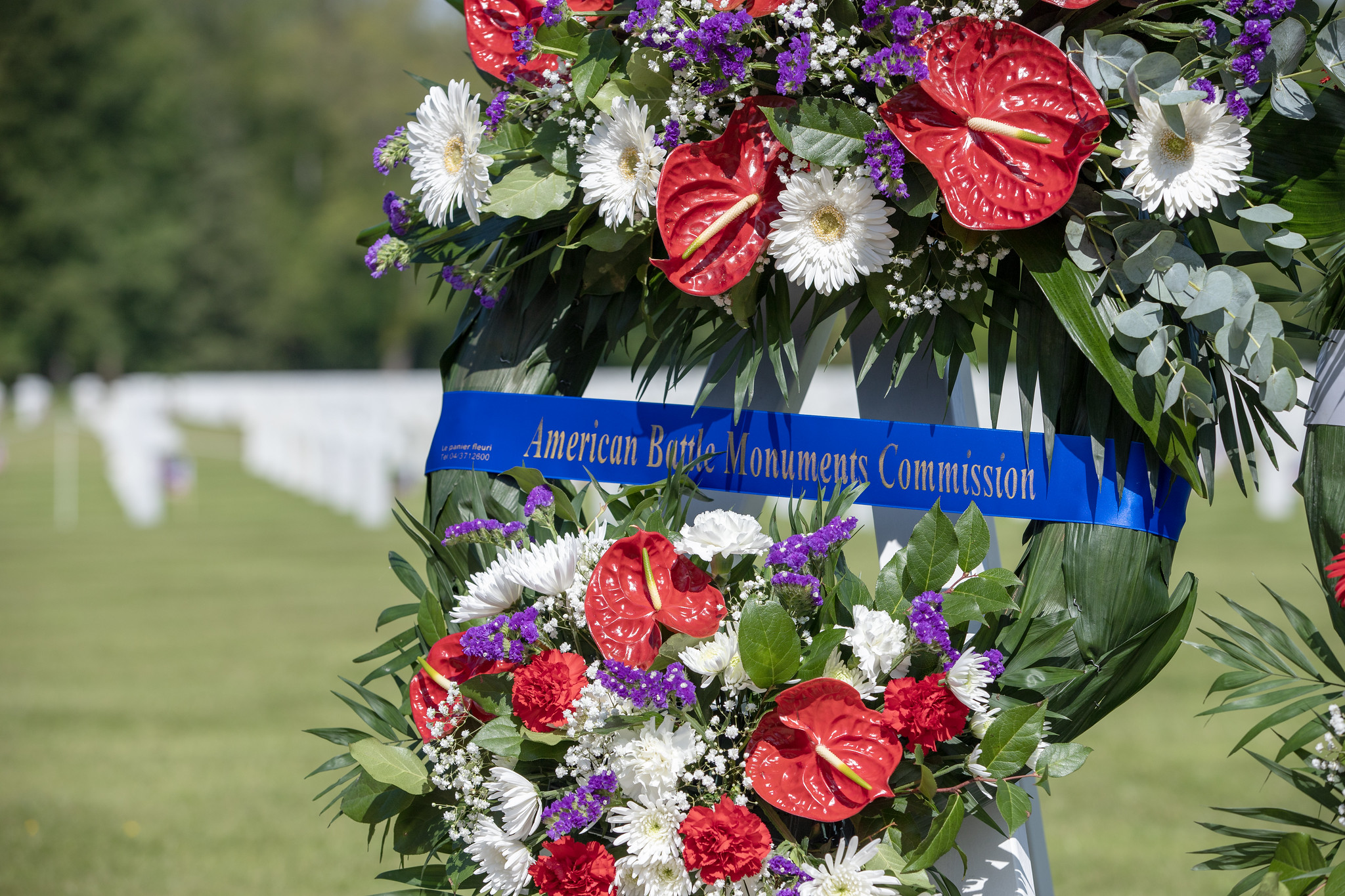 flower wreath with blue ribbon with text that reads American Battle Monuments Commission.