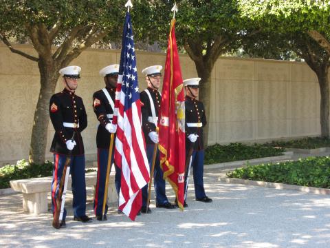 Marines stand with flags and weapons in front of the Wall of the Missing.