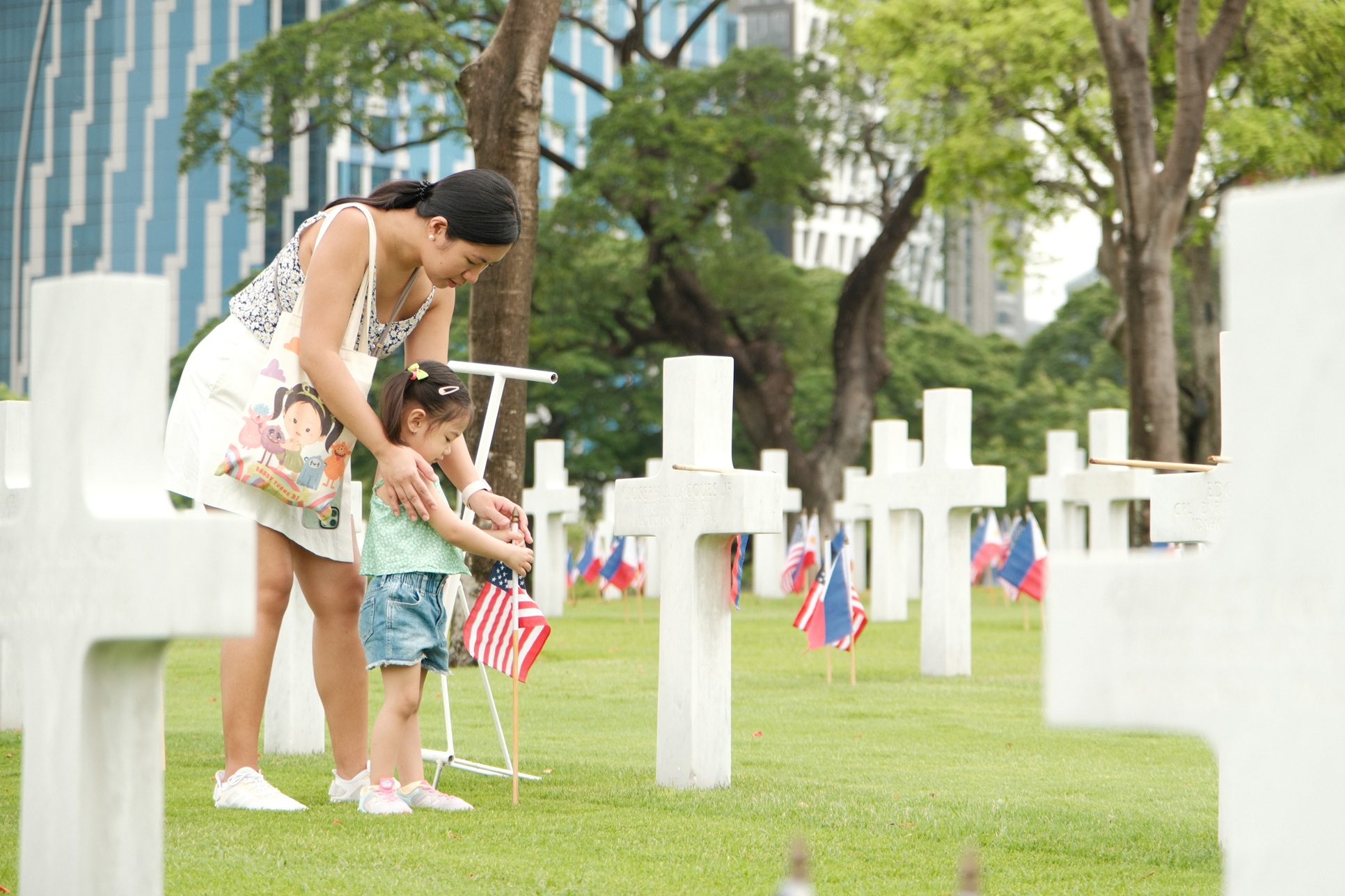A mother and daughter place small American flags in front of headstones of World War II American fallen buried at Manila American Cemetery ahead of Memorial Day, 2024. A mother and daughter place small American flags in front of headstones of World War II American fallen buried at Manila American Cemetery ahead of Memorial Day, 2024.