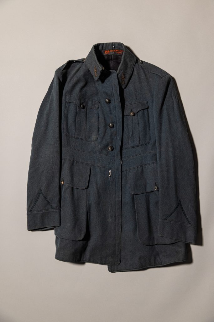 Dark blue military-style uniform jacket with button front, flap pockets, and decorative collar insignia displayed against a light background.