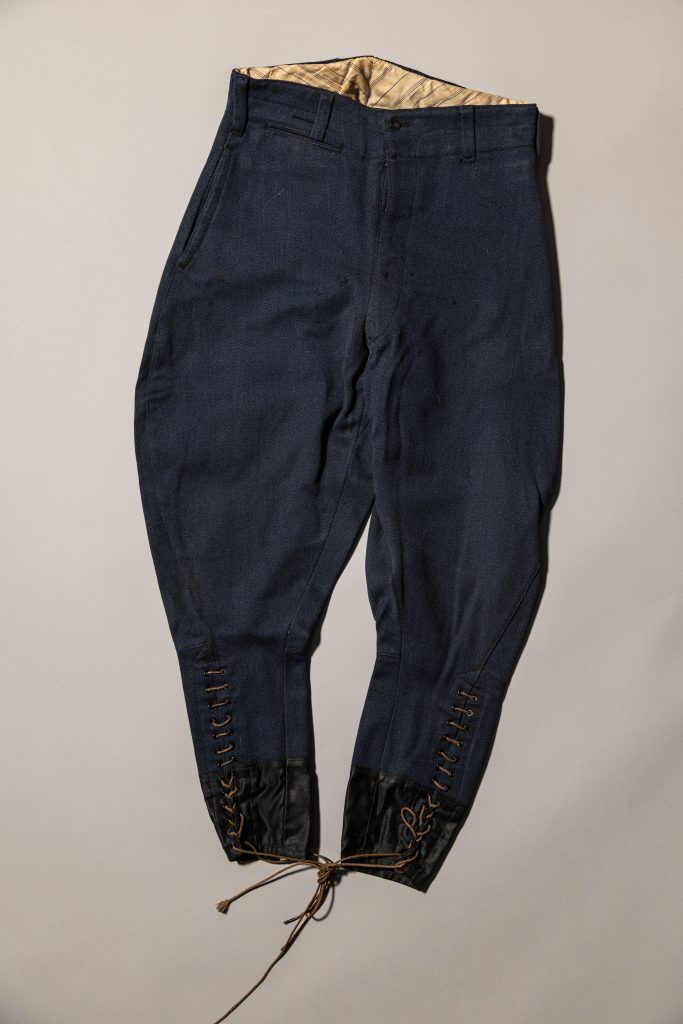 Dark blue military riding breeches with lace-up cuffs and black leather ankle reinforcements displayed against a light background.