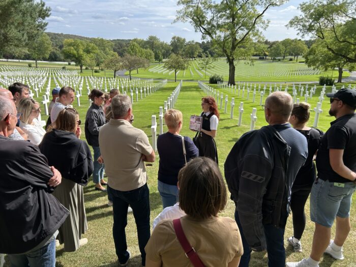 Visitors gathering around the guide at Lorraine American Cemetery during European Heritage Days 2026 with the plots and some trees in the backrgound.