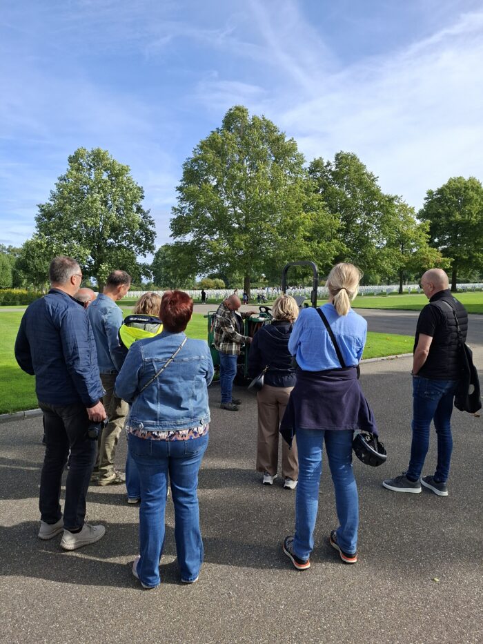 Visitors gathering around a gardener at Netherlands American Cemetery for European Heritage days with the plots in the background and some trees.