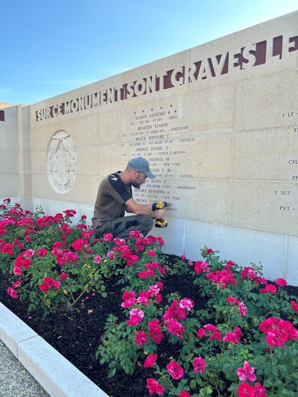 EPAC places a rosette for identified WWII soldier A man drills a hole in a stone wall at Epinal American Cemetery