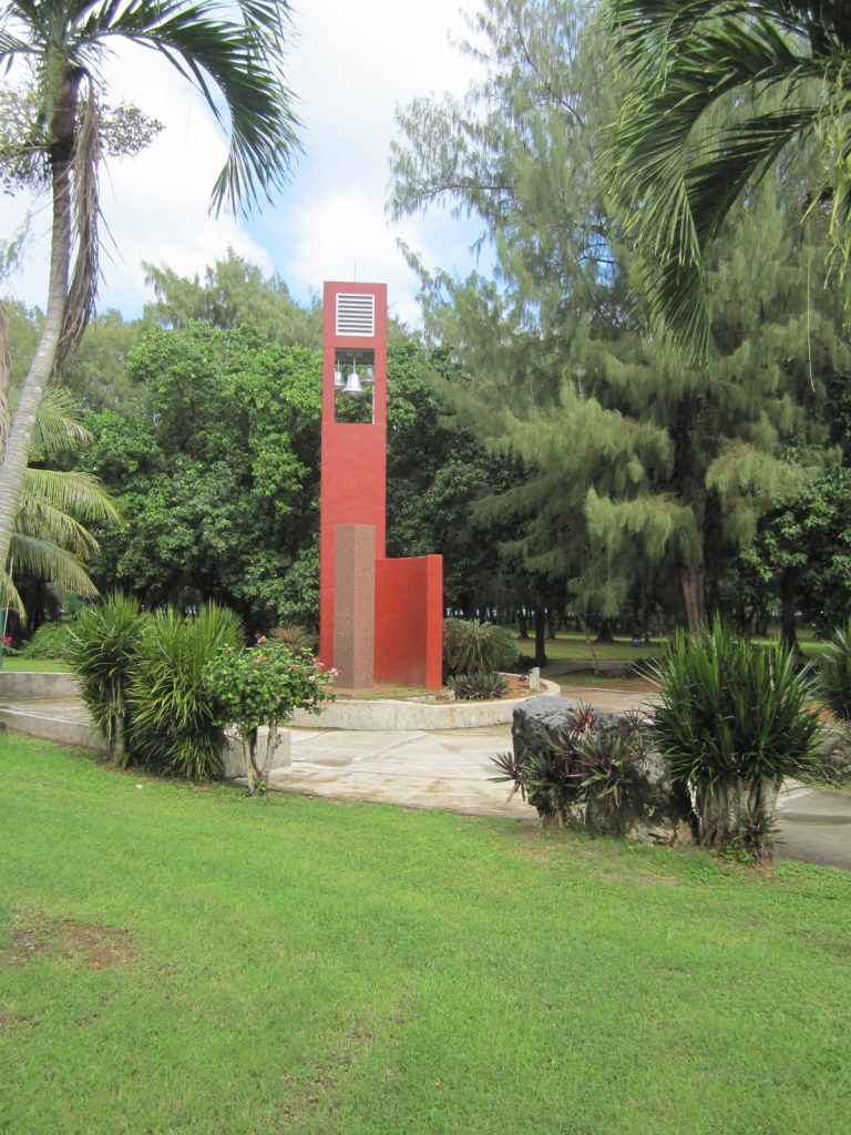 Amidst greenery, a memorial area includes a granite column.