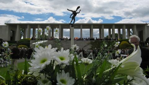 Blooming flowers with memorial and statue in background.