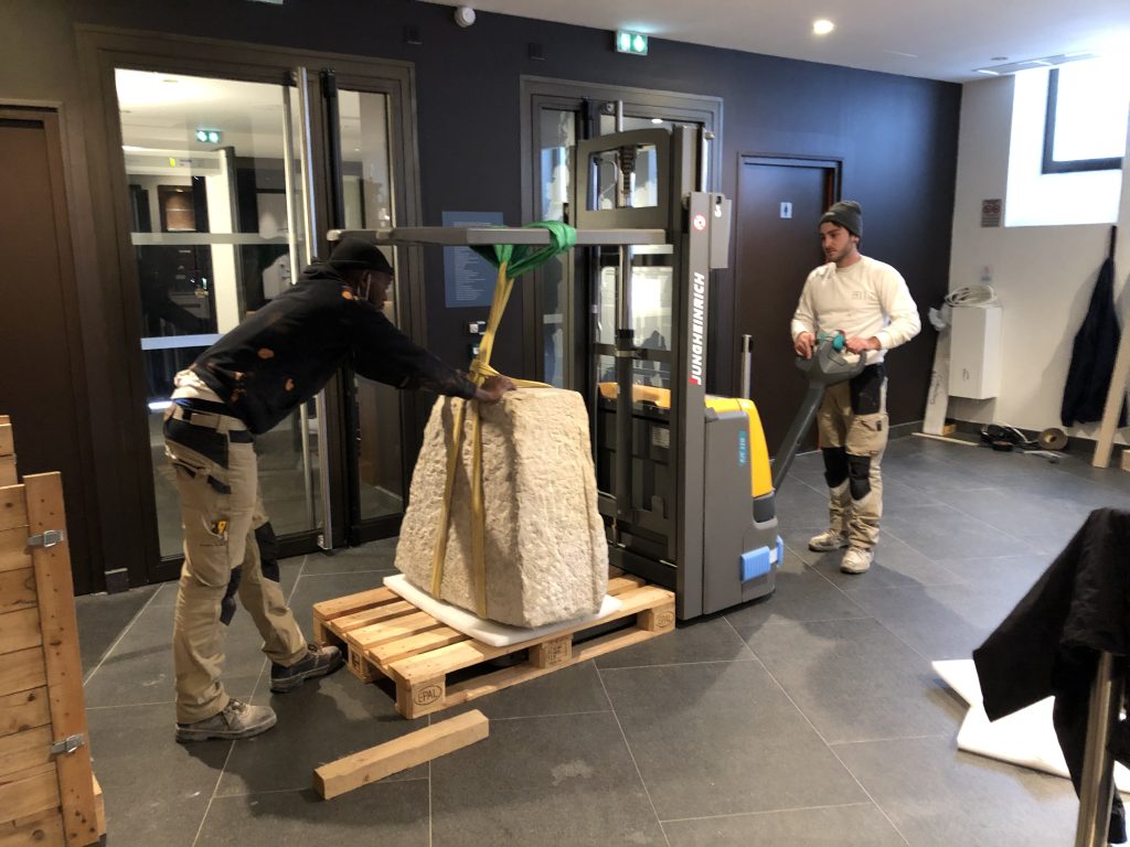 Workers use a pallet stacker and lifting straps to move the Chateau-Thierry Bridge keystone from a shipping pallet into the monument’s visitor center. The historic stone is positioned for installation in its future exhibit location.