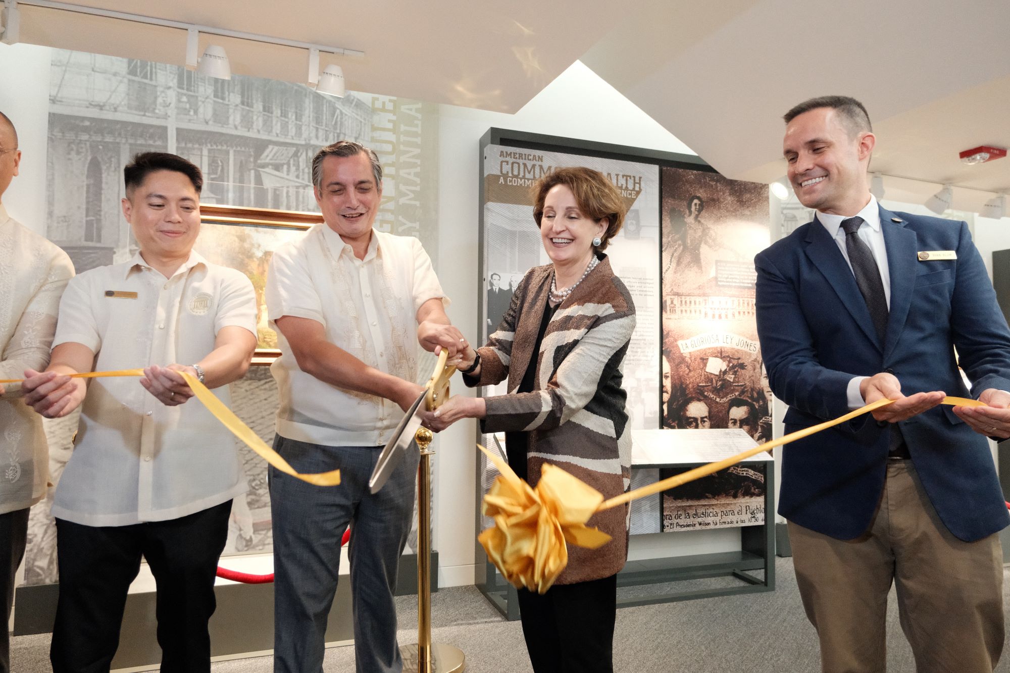 Four people cut a gold ribbon in front of the art exhibit to kick off the event.