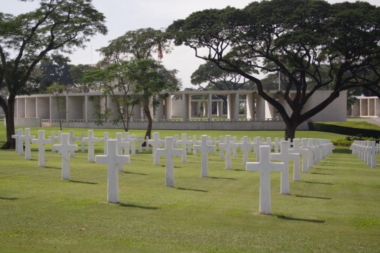 Picture of Manila American Cemetery with headstones in the front of the picture and the memorial in the back. Credit: American Battle Monuments Commission/ Robert Uth.