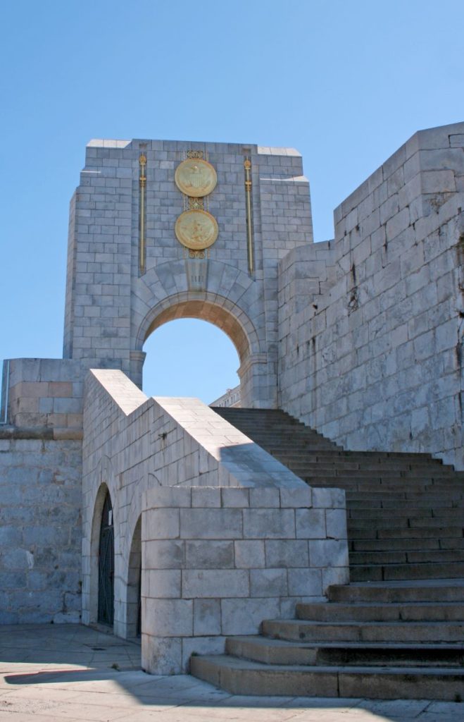 Stone stairs lead up to the Naval Monument at Gibraltar featuring two gold seals over a curved arch.