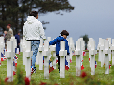Man and young boy walk among the headstones at Normandy American Cemetery.