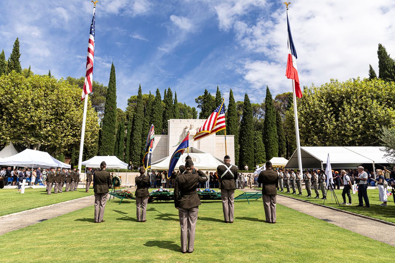 Commemorating Operation Dragoon Soldiers facing the monument and ceremony guests salute during the playing of taps