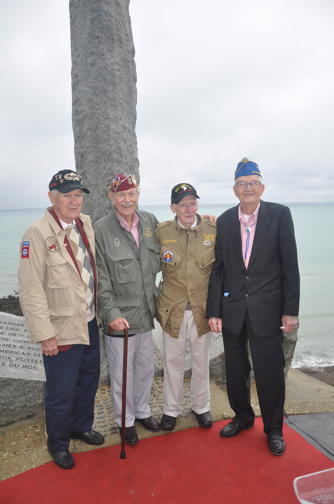 D-Day veterans stand at the foot of the Pointe du Hoc Ranger Memorial. Image courtesy of Mark Easton.