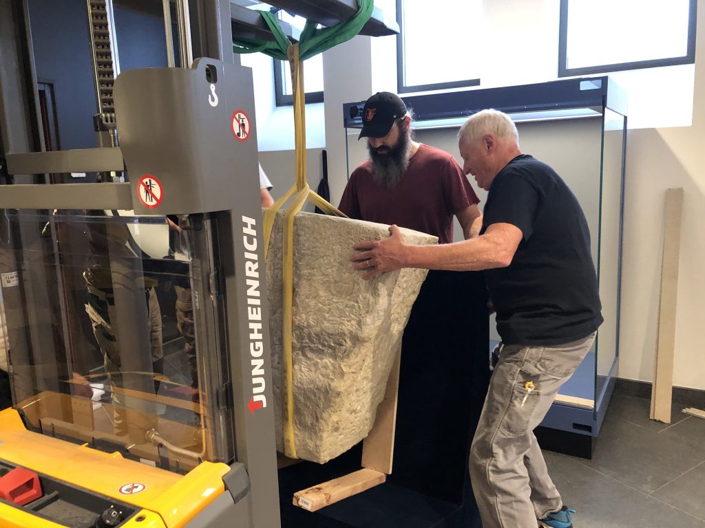 Installation team members guide the Chateau-Thierry Bridge keystone as it is suspended by lifting straps and carefully maneuvered into a display case at the Chateau-Thierry Monument.