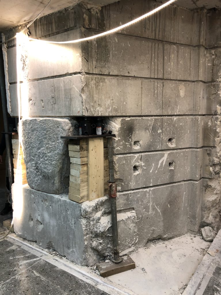 The Chateau-Thierry Bridge keystone remains embedded within a masonry support while engineers install hydraulic jacks, wood cribbing, and temporary bracing to stabilize the surrounding structure during preservation and removal preparations.