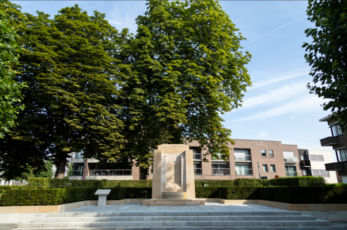The Audenarde Monument on the top of a few greay steps in the middle of the city with buildings behind it.