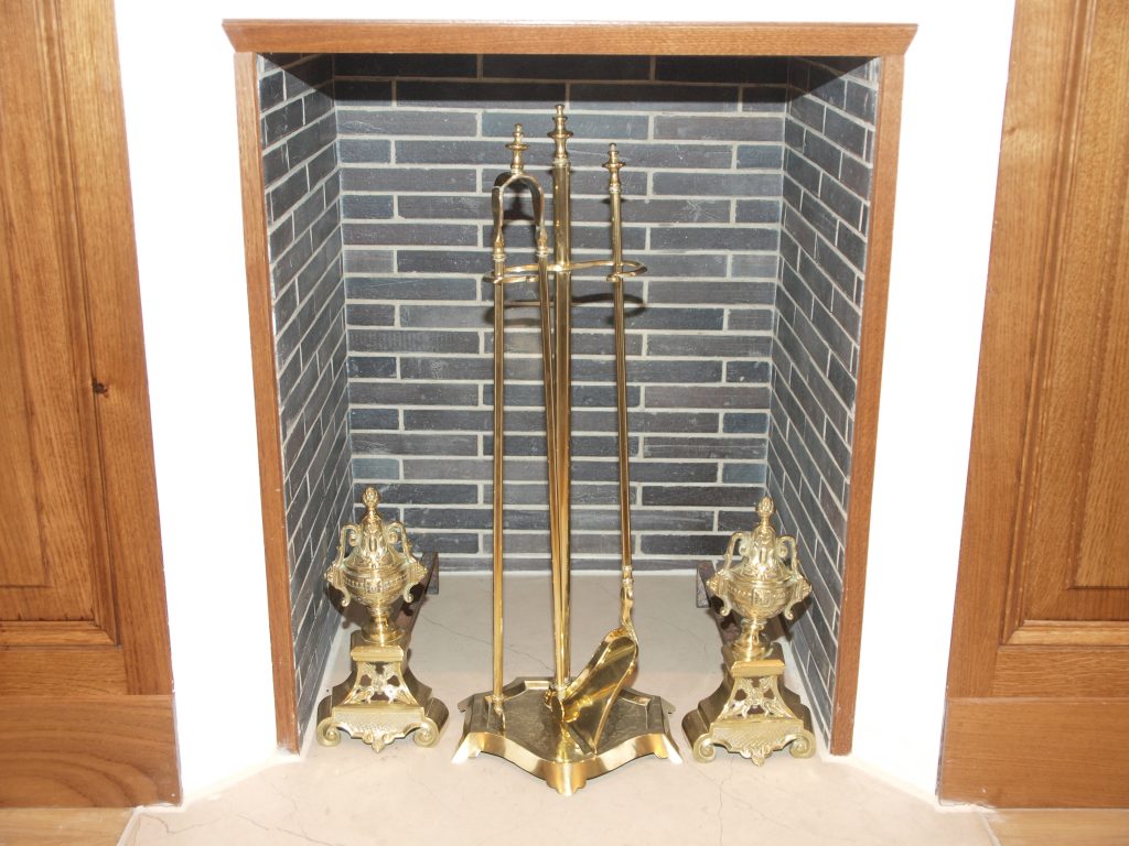 Brass fireplace tool set and matching andirons displayed in a tiled fireplace.