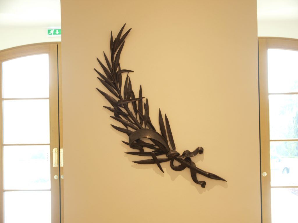 Decorative wall-mounted sculpture of a laurel branch tied with a ribbon, displayed between two glass-paneled doors.