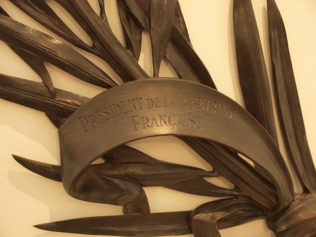 Close-up of a decorative laurel branch sculpture with a ribbon engraved “Président de la République Française.”