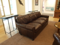 Brown leather sofa displayed in a reception room with large windows, side tables, and historic furnishings.